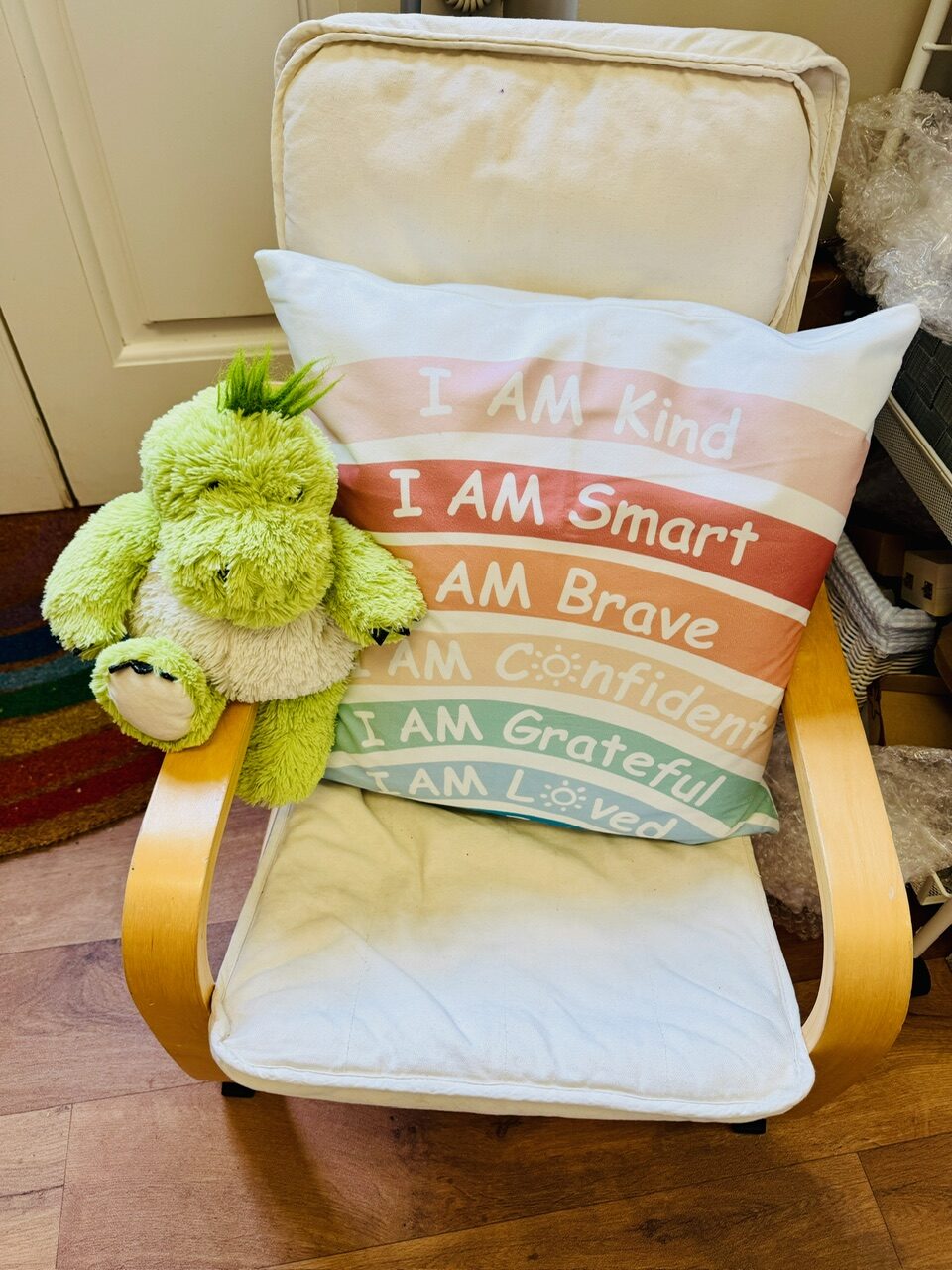 A cushion reading I am kind, smart, brave, confident, grateful and loved, with a soft green toy beside it