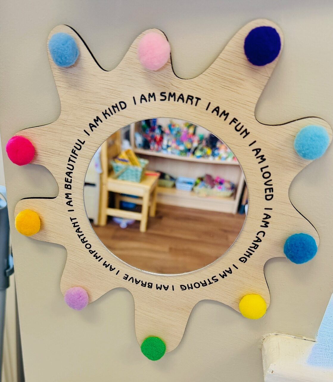 A sunburst mirror edged with pom-poms and kind affirmations like I am kind and I am brave