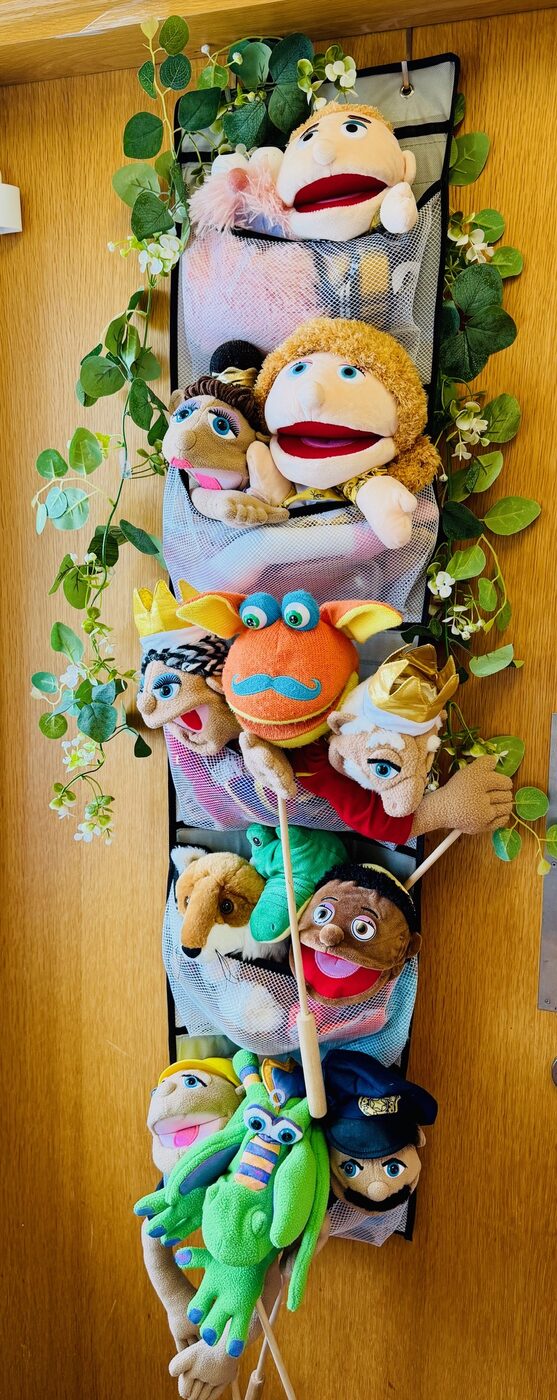 A hanging rack of colourful hand puppets framed by trailing green leaves